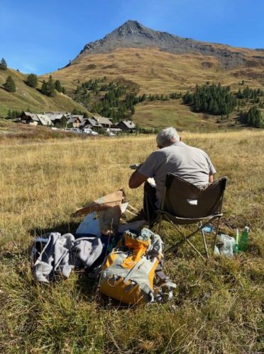 photo d'un homme assis peignant un paysage d'alpage